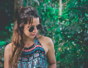 Portrait of young woman wearing sunglasses standing against trees