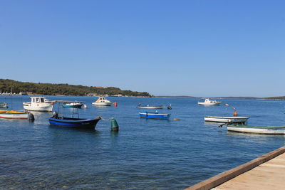 Boats in calm blue sea against clear sky