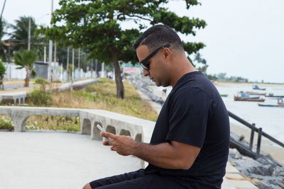 Man wearing sunglasses using mobile phone by sea against sky