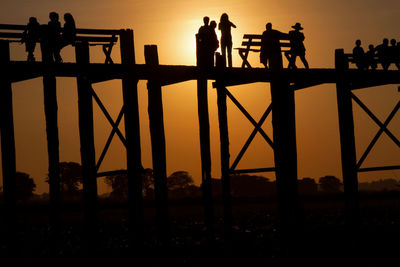 Low angle view of silhouette people on u bein bridge during sunset against sky