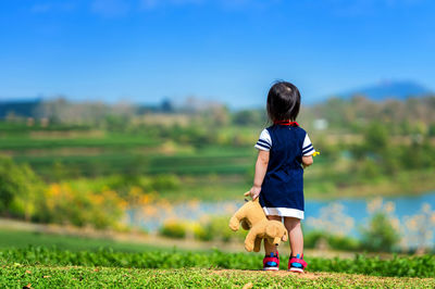 Rear view of girl with toy standing on grassy field