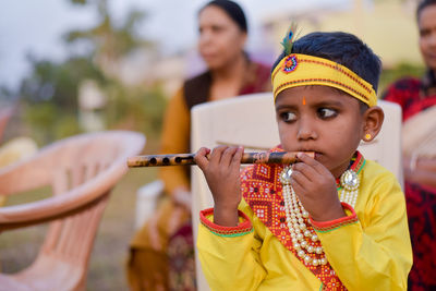 Close-up of thoughtful boy wearing costume while playing flute on chair