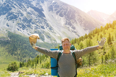 Portrait of man with arms outstretched against mountain on sunny day