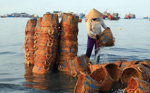 Woman washing old whicker baskets in sea