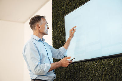 Mature businessman pointing at touch screen computer monitor in coworking office