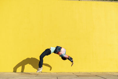 Acrobat jumping somersaults in front of yellow wall