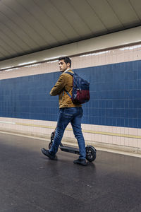 Man in stylish outfit walking with electric scooter in the underground