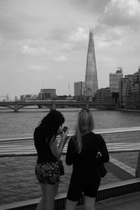 Rear view of women on bridge over thames river against shard london bridge in city