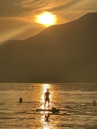 Silhouette person on sea against sky during sunset