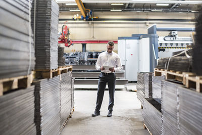 Businessman with tablet standing on factory shop floor