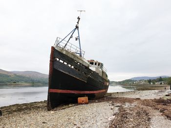 Abandoned ship moored on beach against sky