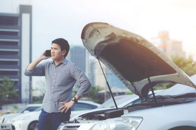 Man talking on phone while standing by broken car