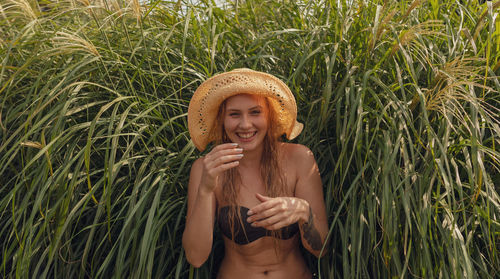 Portrait of happy young woman wearing hat while standing against plants