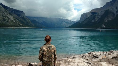 Rear view of woman standing at lakeshore against mountains