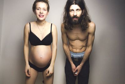 Portrait of shirtless man with pregnant woman against gray background