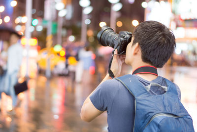 Rear view of man photographing illuminated city street at night