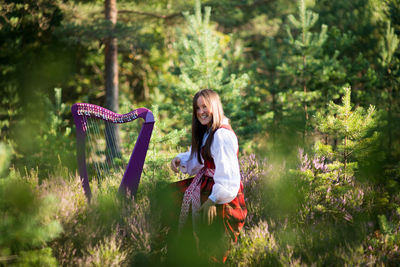 Woman playing harp against trees in forest