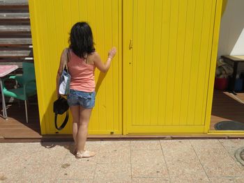 Rear view of woman standing by yellow door