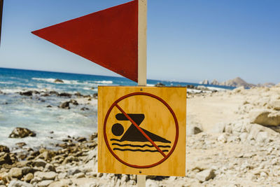 Close-up of warning sign on beach against sky