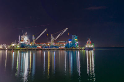Illuminated commercial dock by sea against sky at night