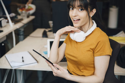 Portrait of happy female computer hacker using digital tablet while sitting in office