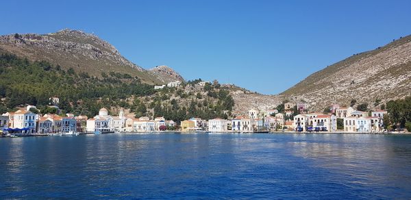 Scenic view of lake and buildings against clear blue sky