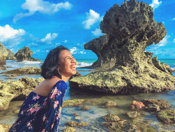 Young woman on rock at beach against sky