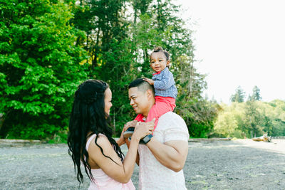 Side view of a boy sitting on his dad's shoulders while mom looks on