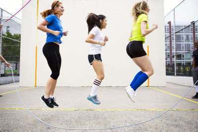 Side view of women performing double dutch against wall