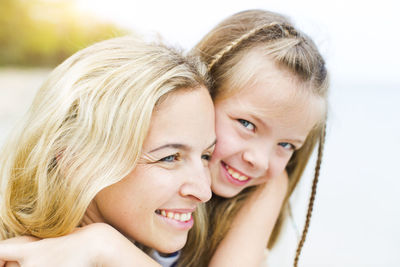 Close-up portrait of smiling girl with mother at beach