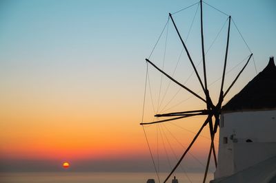 Traditional windmill by sea against clear sky during sunset