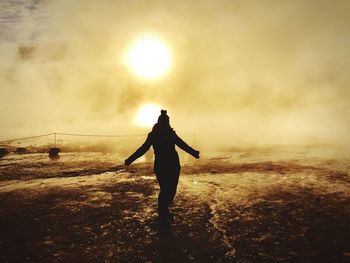 Rear view of silhouette woman standing on land against sky during sunset