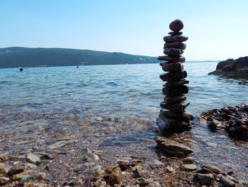 Stack of stones at lakeshore against clear blue sky