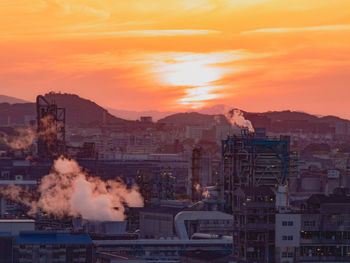 Smoke emitting from factory against sky during sunset