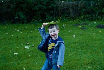 Portrait of cute boy holding leaf on head at grassy field