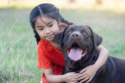 A lovely southeast asian child girl in red outfits plays with her big dog in the back or front yard