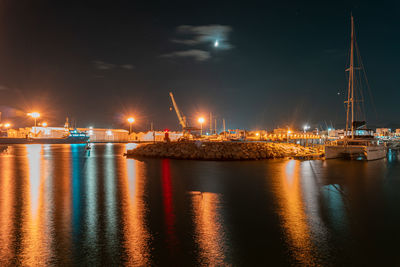 Illuminated commercial dock by sea against sky at night