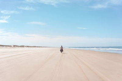 Rear view of woman walking at beach against sky