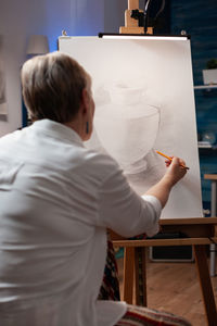 Rear view of woman sketching on canvas