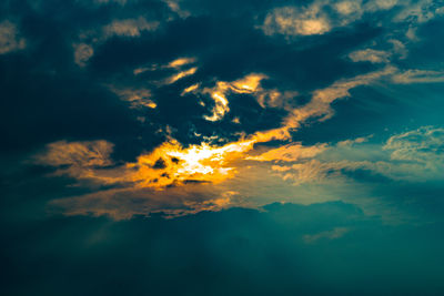 Low angle view of sunlight streaming through clouds