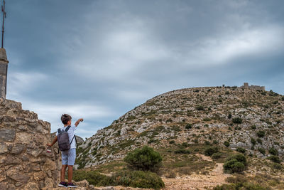 Side view of man standing on rock against sky