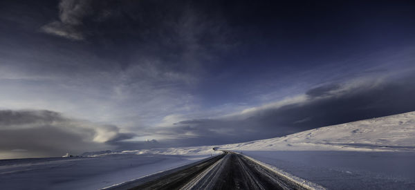 Road leading towards snow covered mountain against sky