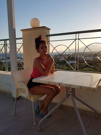 Portrait of woman sitting on railing against sky