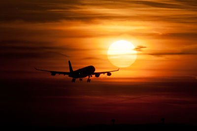 Silhouette airplane flying against orange sky