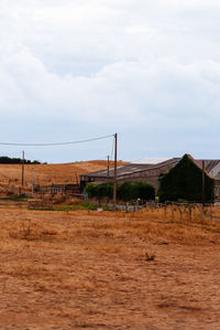 Fence on field by houses against sky