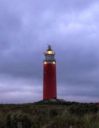 Lighthouse on field by building against sky