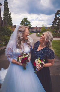 Happy bride and bridesmaid holding bouquet while standing on road