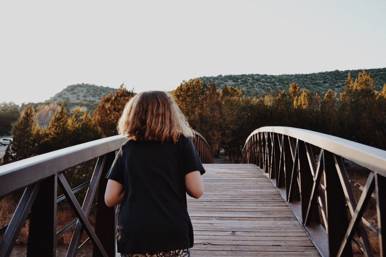 railing, lifestyles, leisure activity, rear view, full length, casual clothing, clear sky, mountain, wood - material, steps, sitting, person, standing, boardwalk, tranquility, relaxation, nature, tranquil scene