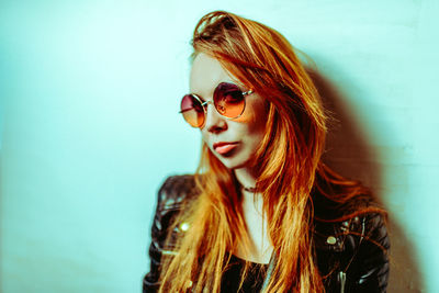 Portrait of young woman wearing sunglasses against wall