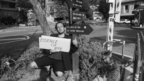 Portrait of man gesturing at information sign by road in city